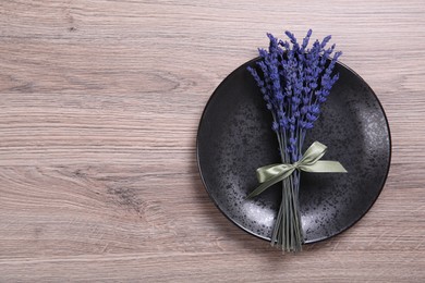 Photo of Bouquet of beautiful preserved lavender flowers and plate on wooden table, top view. Space for text