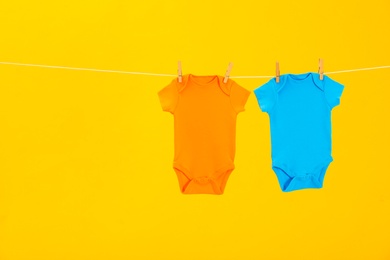 Baby onesies hanging on clothes line against yellow background, space for text