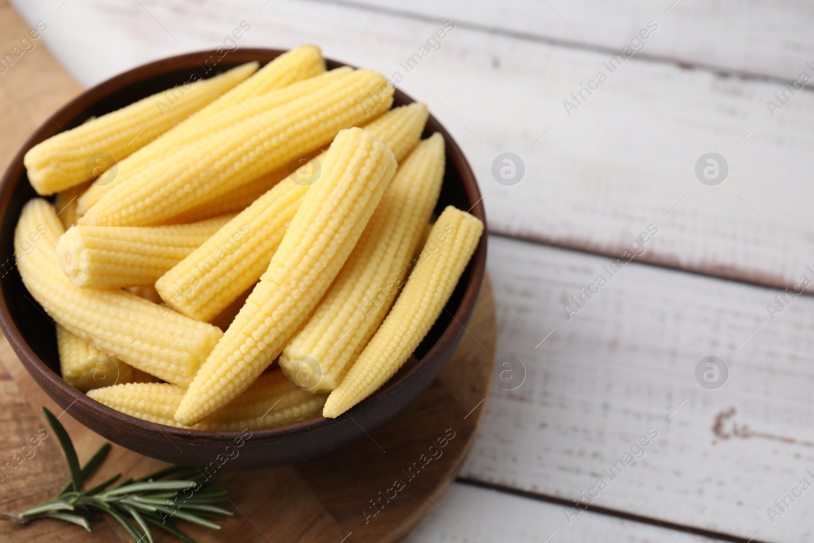 Photo of Tasty fresh yellow baby corns in bowl on white wooden table, space for text