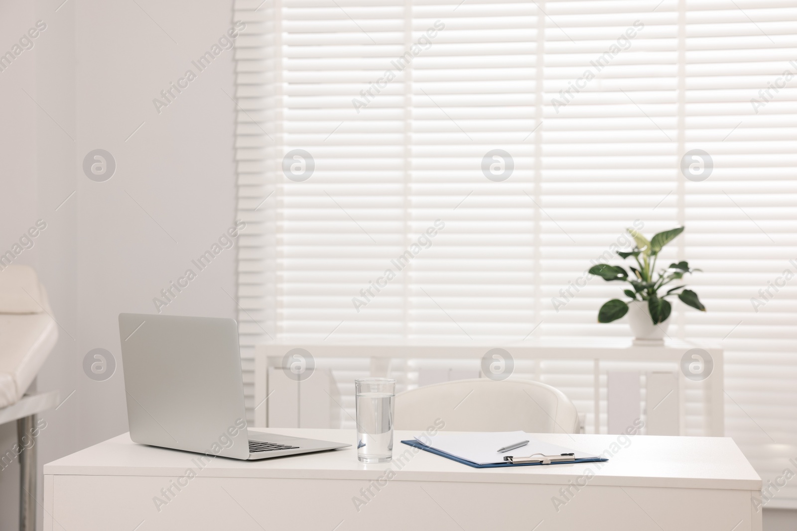 Photo of Doctor's workplace. Laptop, clipboard and glass of water on white table in hospital