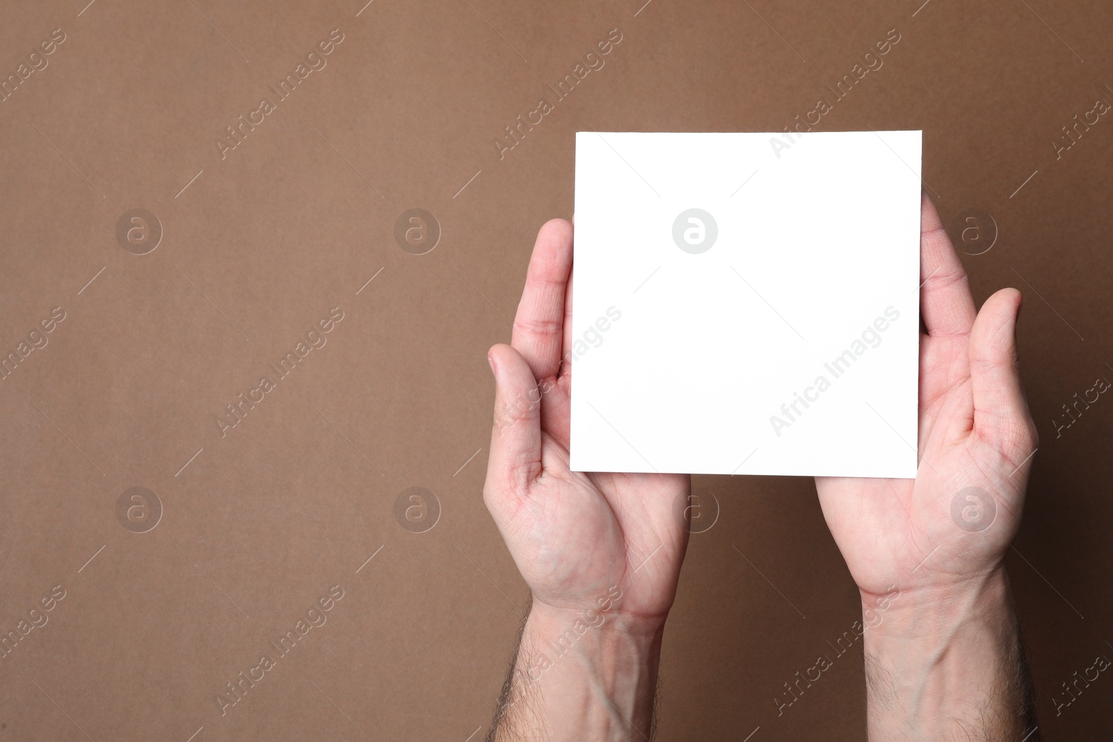 Photo of Man holding sheet of paper on brown background, top view. Mockup for design