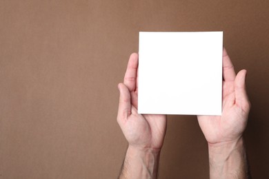 Man holding sheet of paper on brown background, top view. Mockup for design