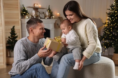 Photo of Happy couple with cute baby and gift in room decorated for Christmas
