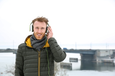 Young man listening to music with headphones outdoors. Space for text