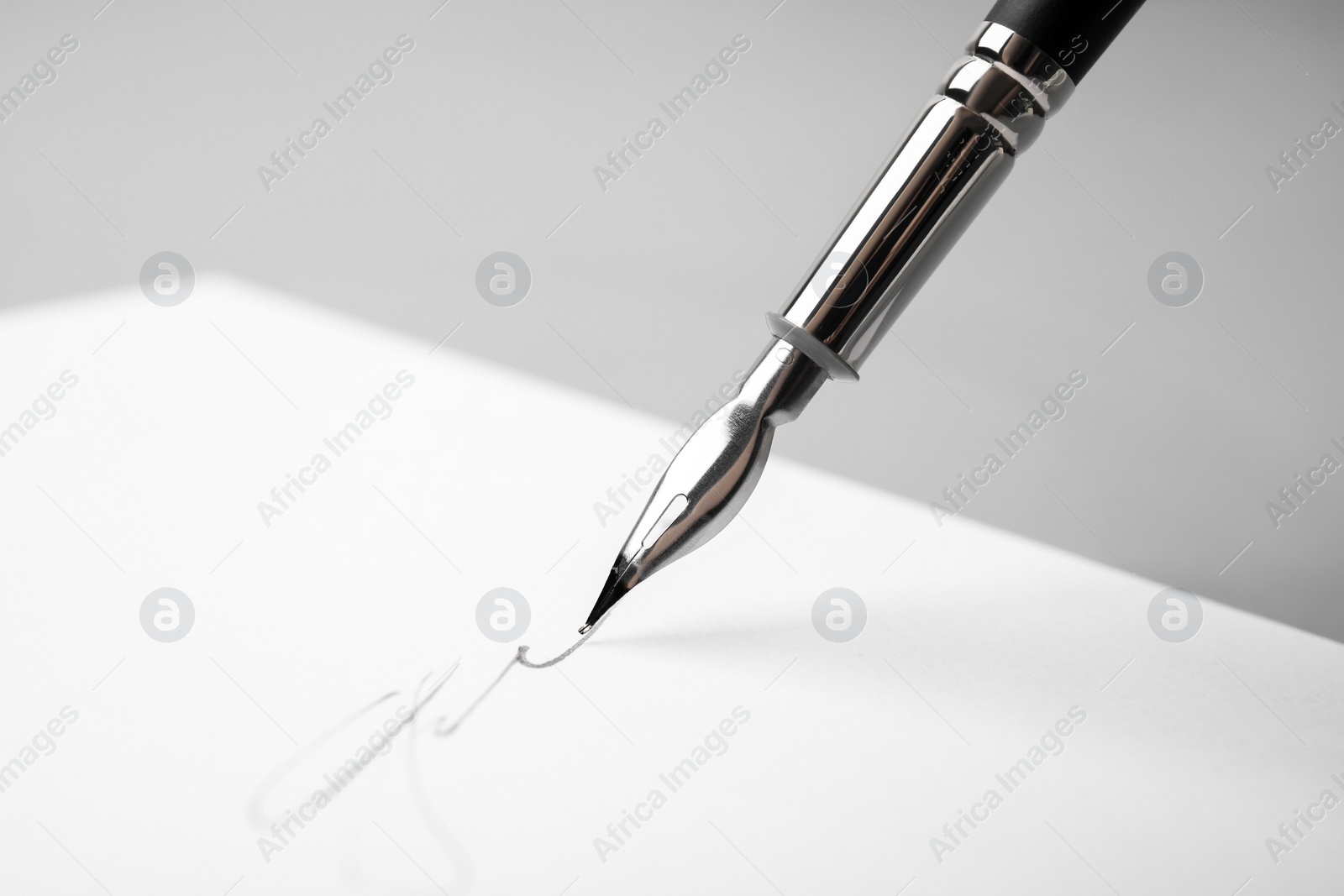 Photo of Signing on sheet of paper with fountain pen against light grey background, closeup