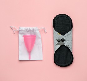 Photo of Reusable cloth pad and menstrual cup on pink background, flat lay