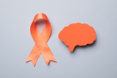 Photo of Orange ribbon and paper brain cutout on light grey background, flat lay. Multiple sclerosis awareness