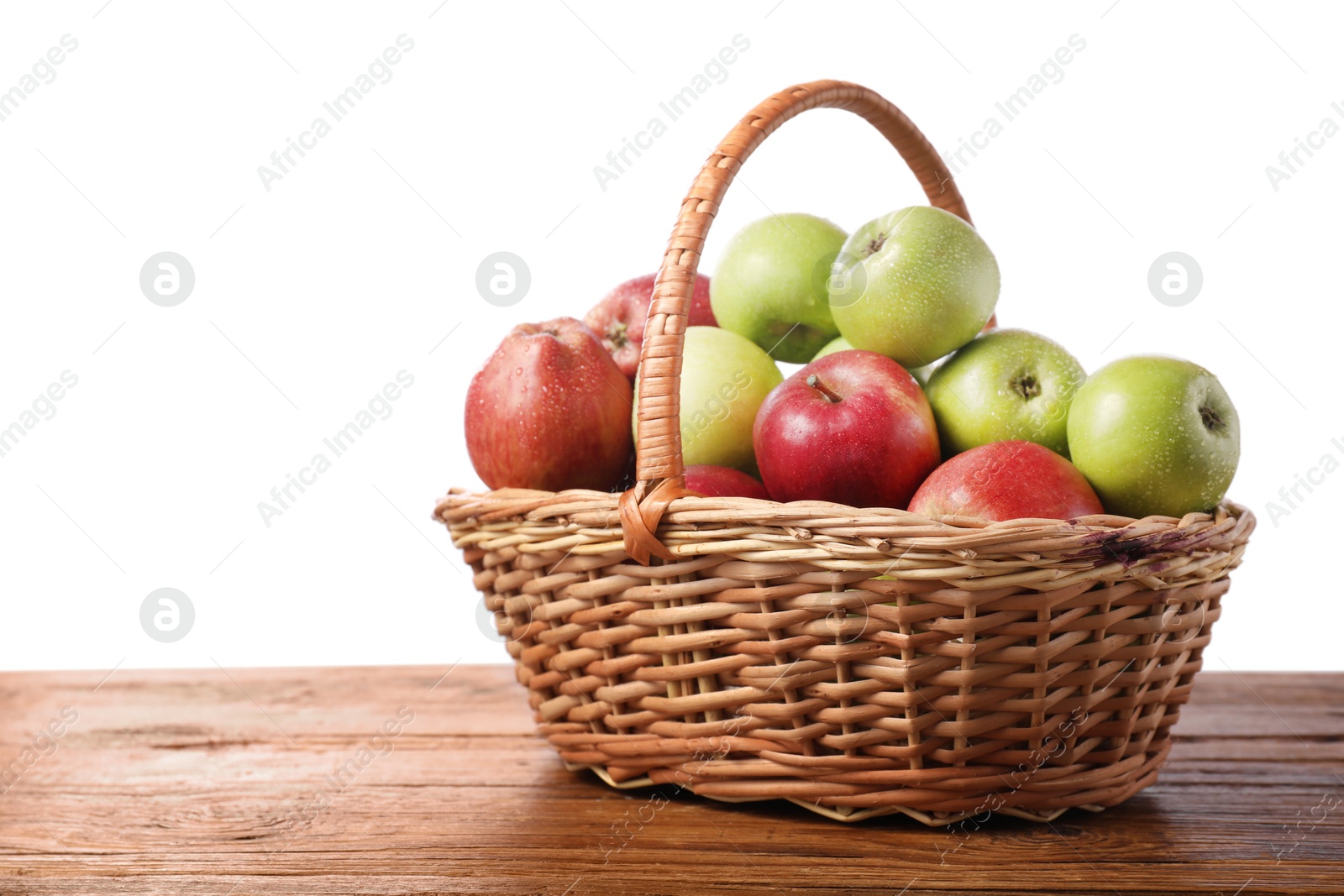 Photo of Fresh red and green apples in wicker basket on wooden table against white background. Space for text