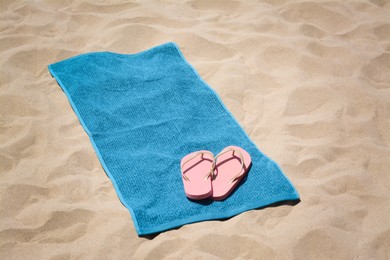 Photo of Soft blue beach towel and pink flip flops on sand. Space for text