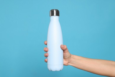 Photo of Woman holding thermo bottle of drink on light blue background, closeup