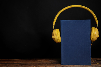 Book and modern headphones on wooden table against black background. Space for text