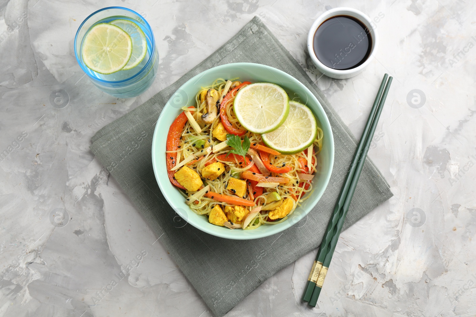 Photo of Stir-fry. Delicious cooked noodles with chicken and vegetables in bowl served on gray textured table, flat lay