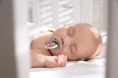 Photo of Cute little baby with pacifier sleeping in crib at home