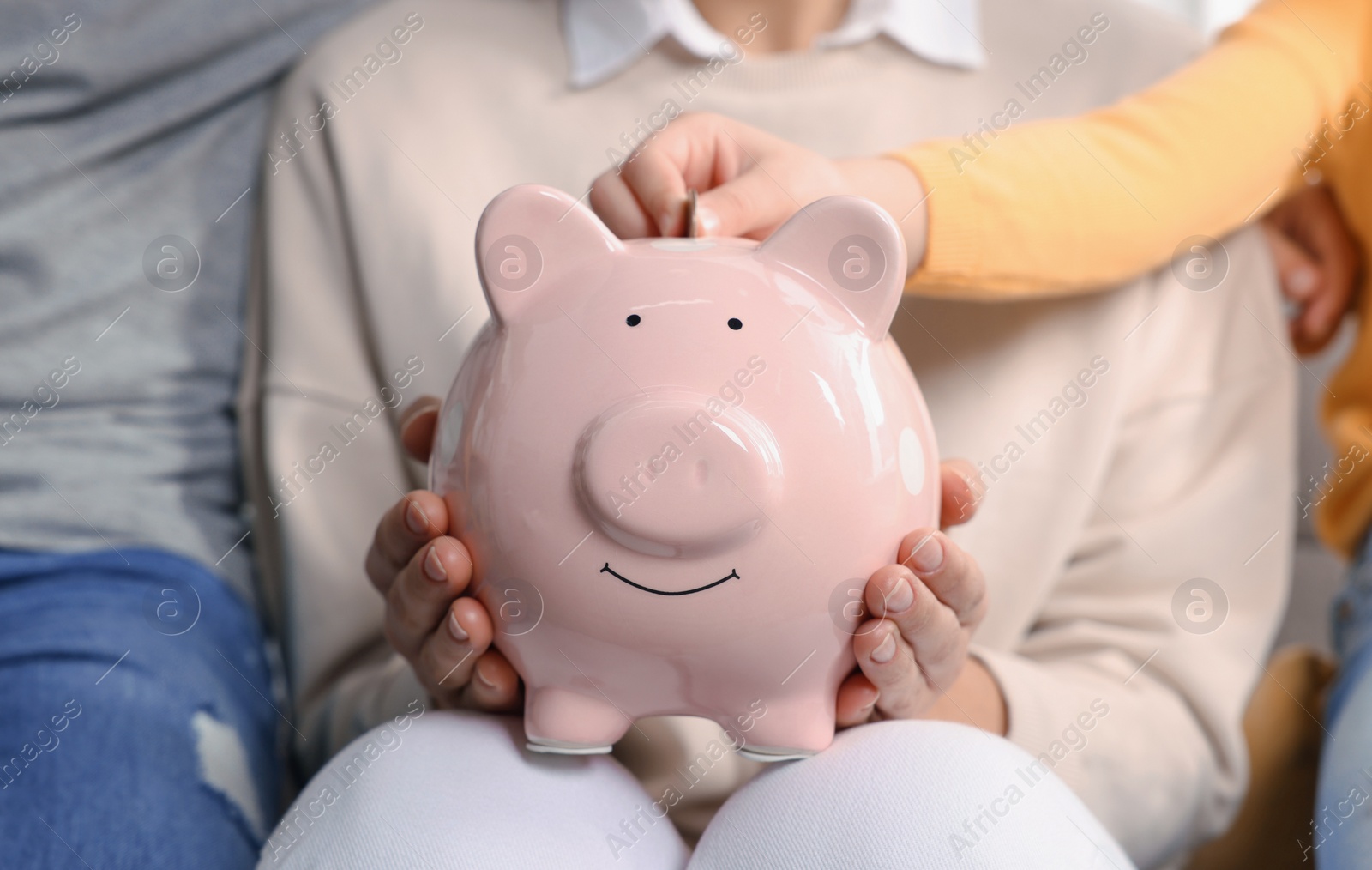 Photo of Family putting coin into piggy bank at home, closeup
