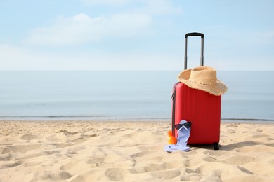 Photo of Red suitcase with beach items on sandy seashore, space for text