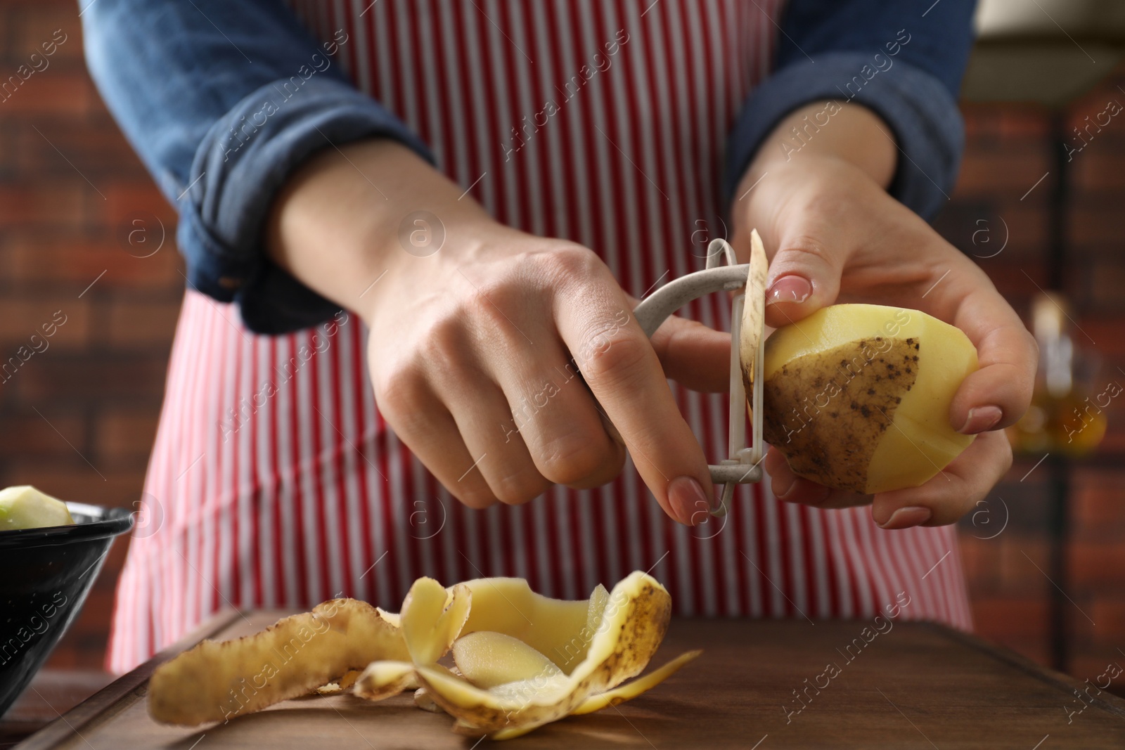 Photo of Woman peeling fresh potato at table indoors, closeup