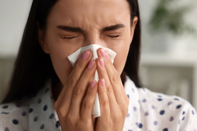 Photo of Suffering from allergy. Young woman blowing her nose in tissue indoors, closeup