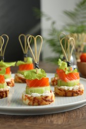 Photo of Tasty canapes with salmon, cucumber, bread and cream cheese on wooden table, closeup