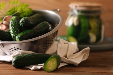 Photo of Fresh cucumbers and colander on wooden table. Pickling vegetables
