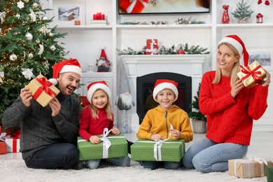 Photo of Happy family in Santa hats with Christmas gifts at home