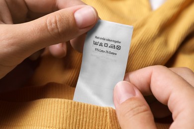Photo of Woman holding clothing label on yellow garment, closeup