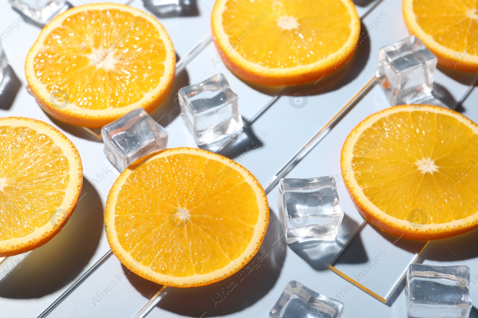 Photo of Slices of juicy orange and ice cubes on light blue background, closeup