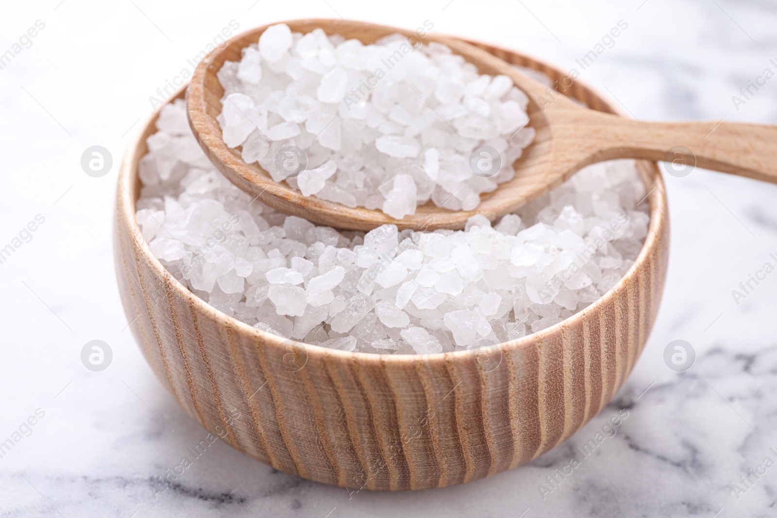 Photo of Bowl and spoon with white sea salt on marble table, closeup. Spa treatment