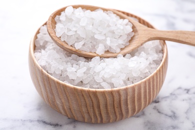 Photo of Bowl and spoon with white sea salt on marble table, closeup. Spa treatment