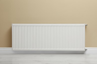 Photo of Modern radiator on beige wall indoors. Central heating system
