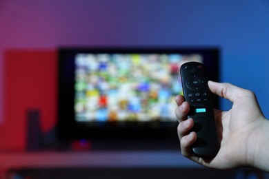 Woman switching channels on TV set with remote control at home, closeup