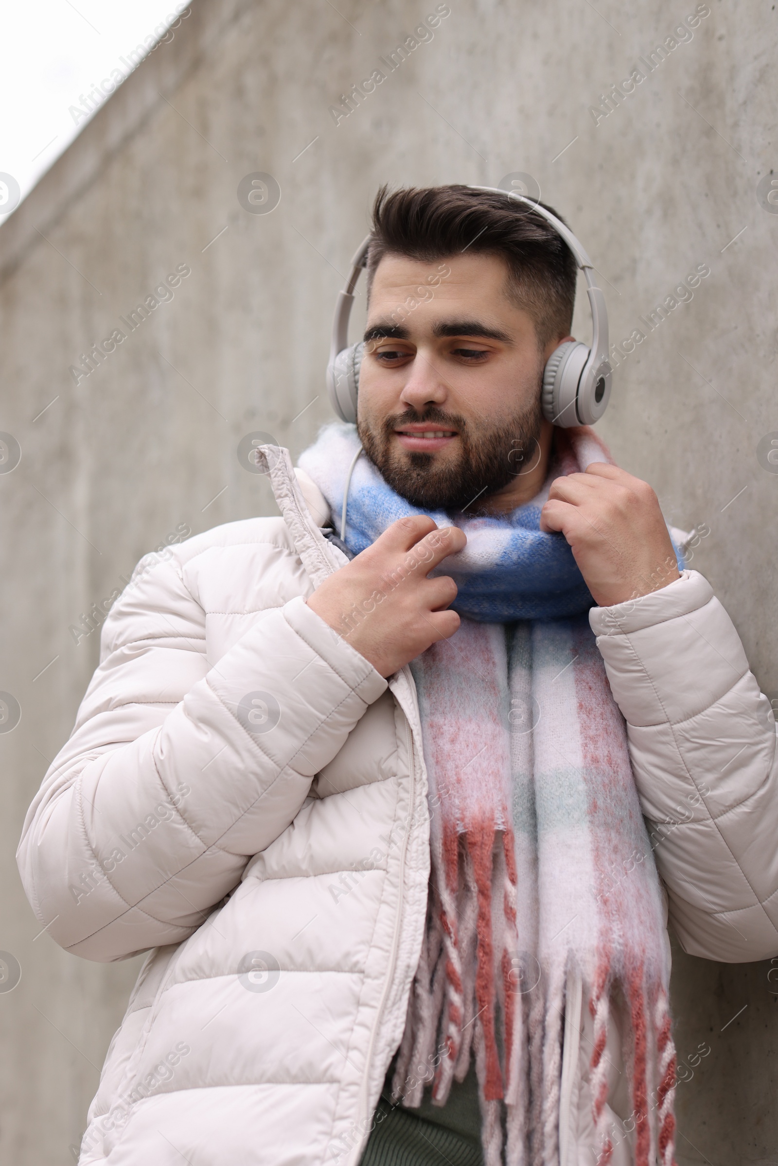 Photo of Handsome man in warm scarf and headphones near wall outdoors