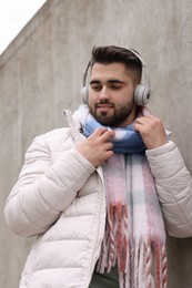 Handsome man in warm scarf and headphones near wall outdoors