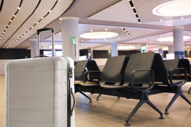 Image of Stylish white suitcase in waiting area at airport terminal