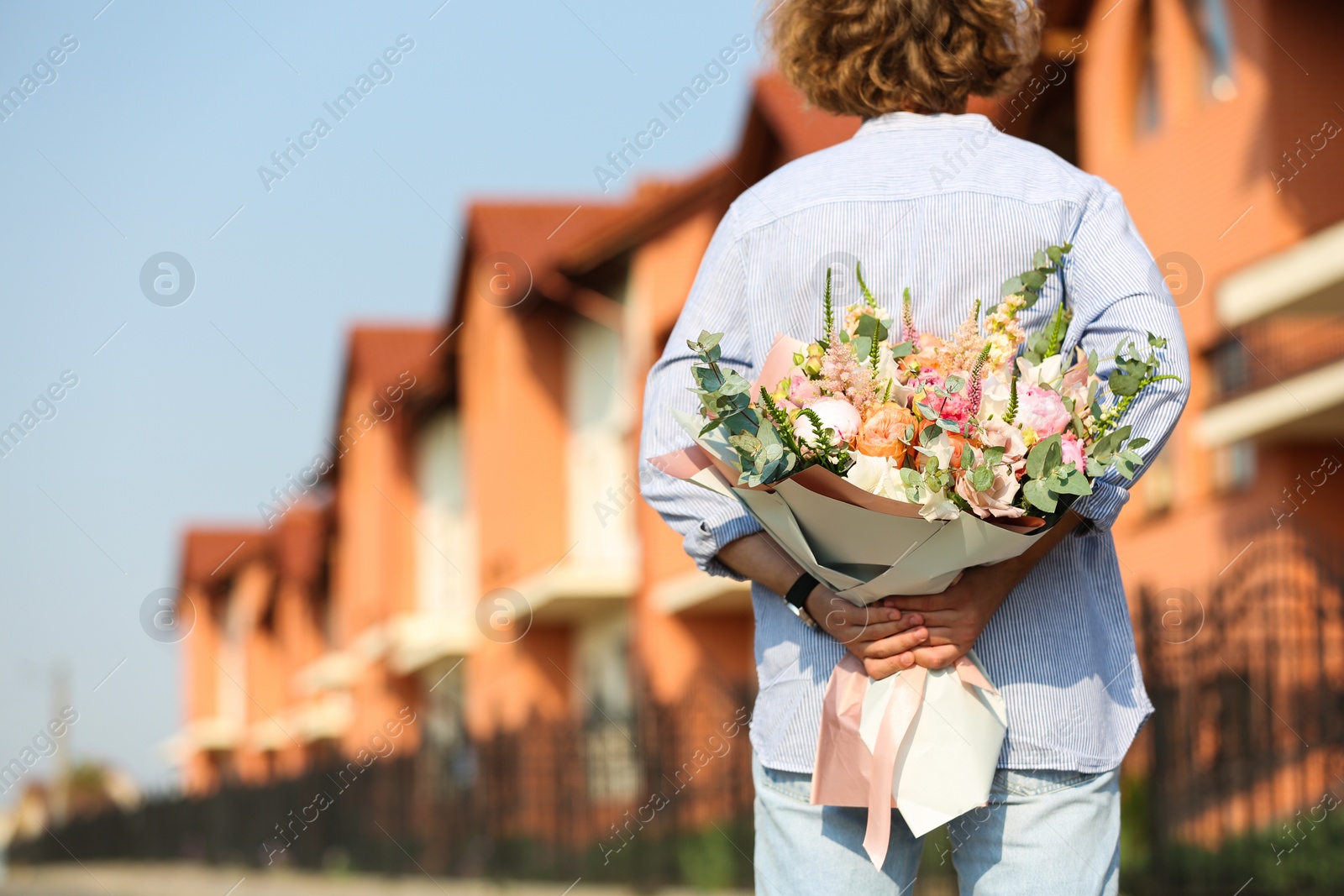 Photo of Man hiding beautiful flower bouquet behind his back on street. Space for text