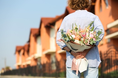 Photo of Man hiding beautiful flower bouquet behind his back on street. Space for text