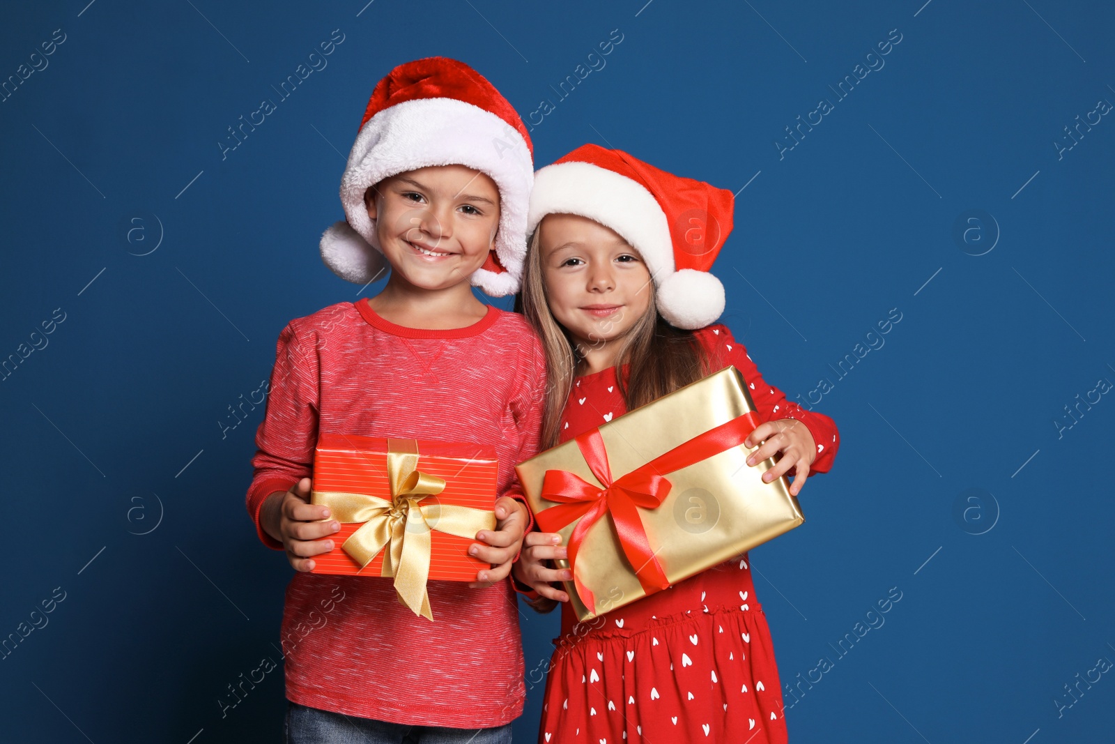 Photo of Happy little children in Santa hats with gift boxes on blue background. Christmas celebration