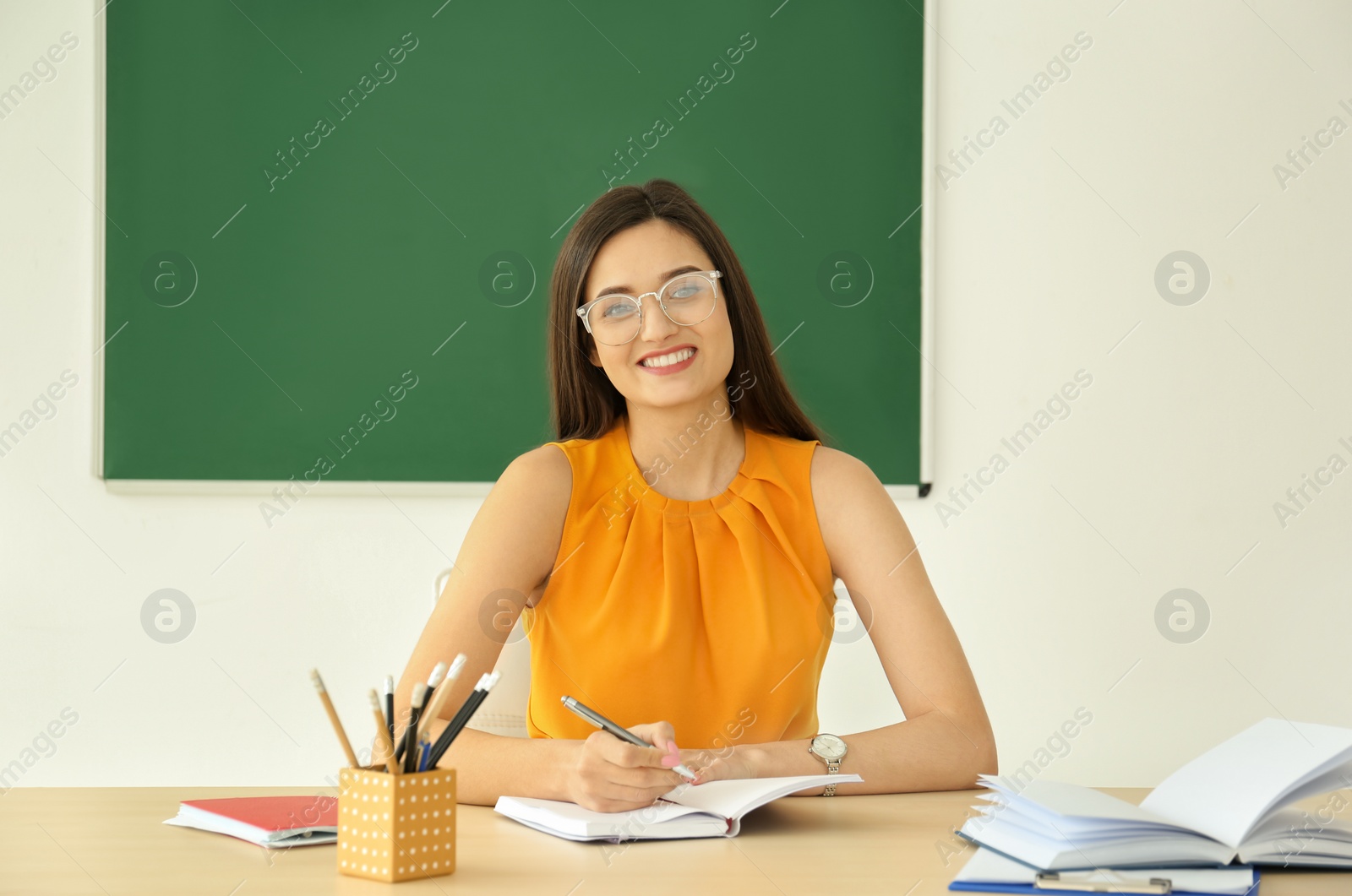 Photo of Young female teacher working at table in classroom