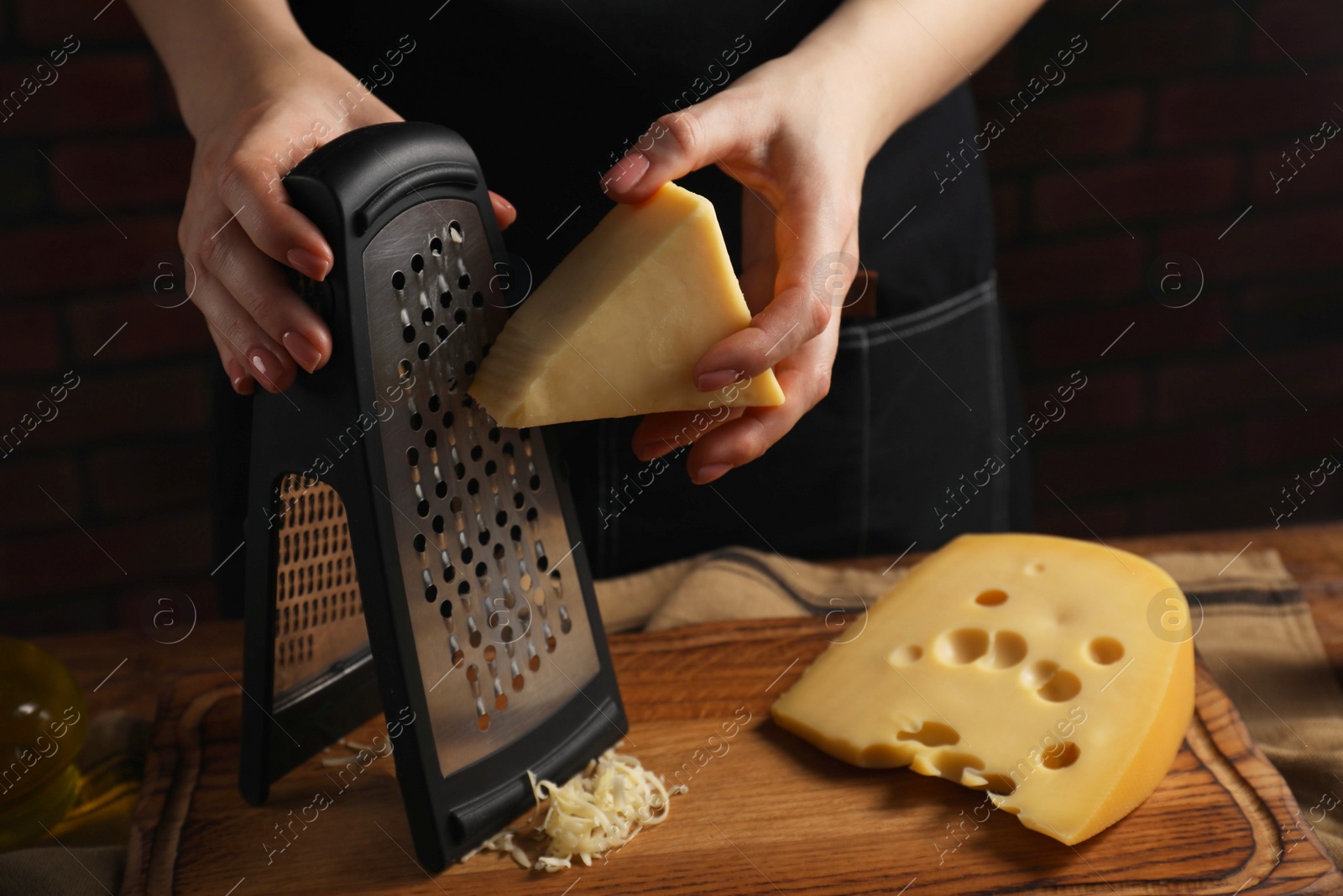 Photo of Woman grating cheese at wooden table, closeup