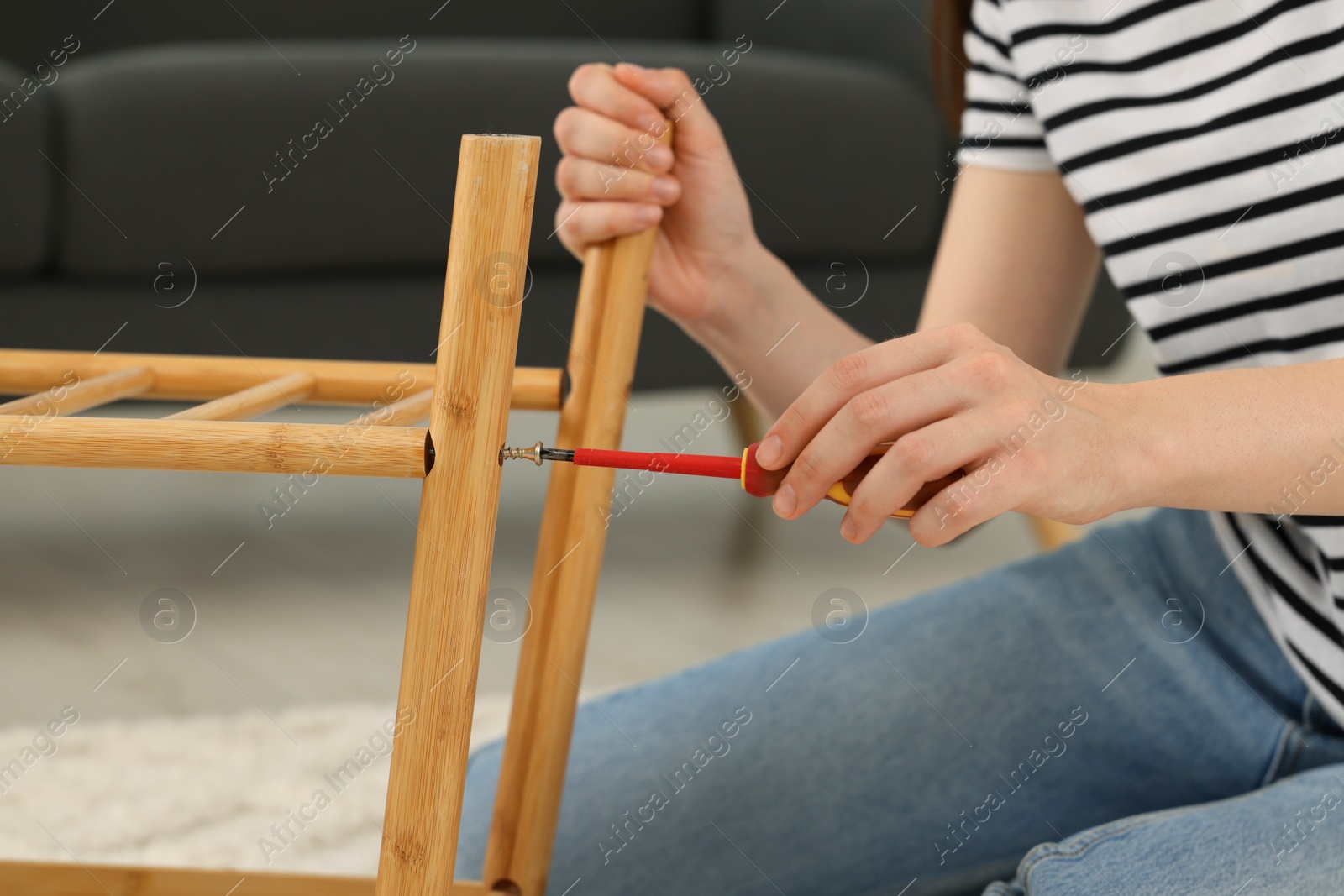 Photo of Woman with screwdriver assembling furniture indoors, closeup