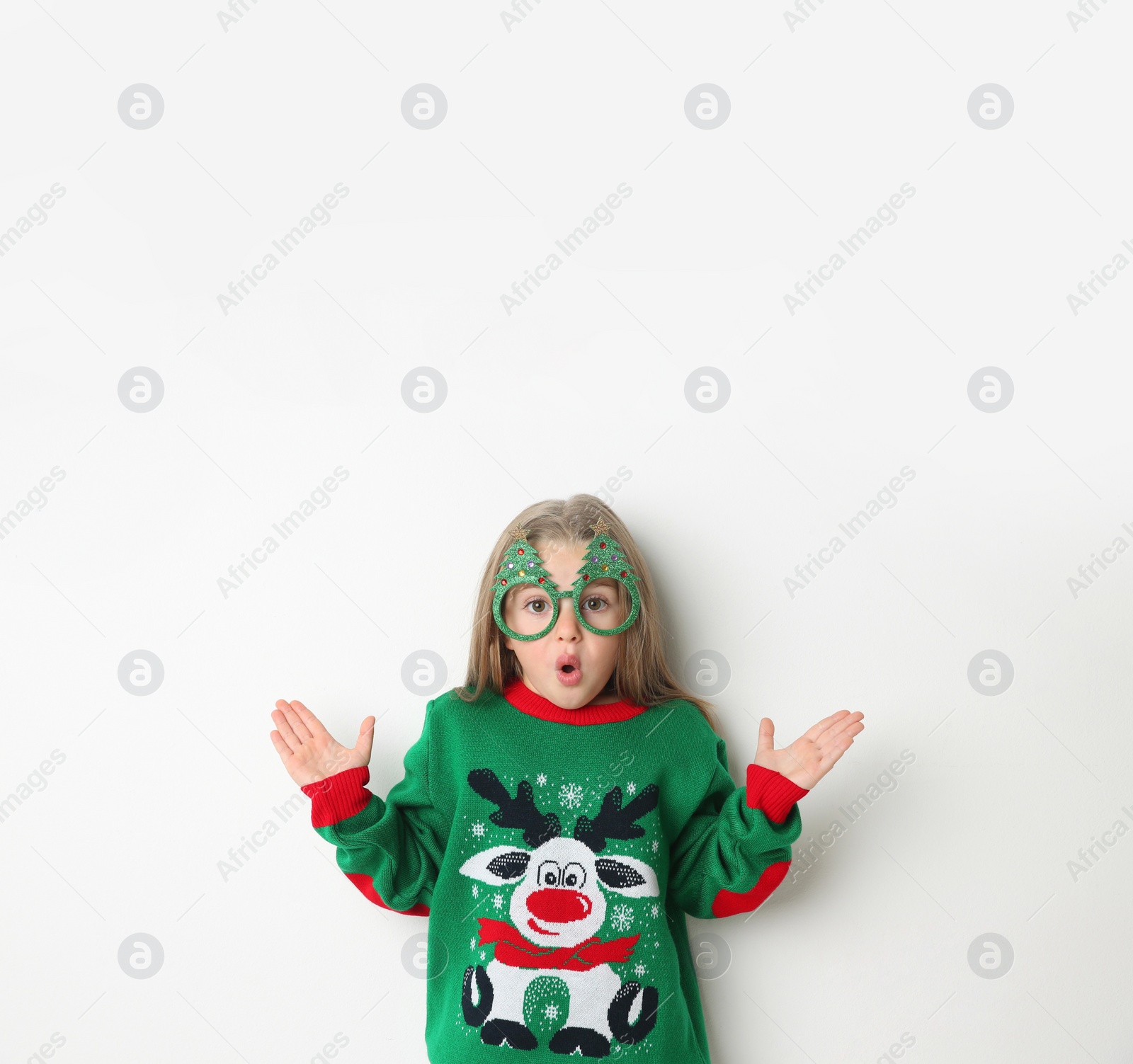Photo of Surprised little girl in Christmas sweater and party glasses on white background