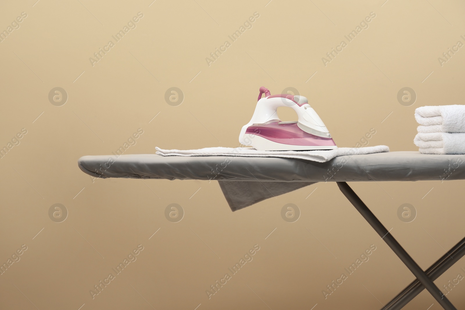 Photo of Modern iron and clean towels on board against beige background