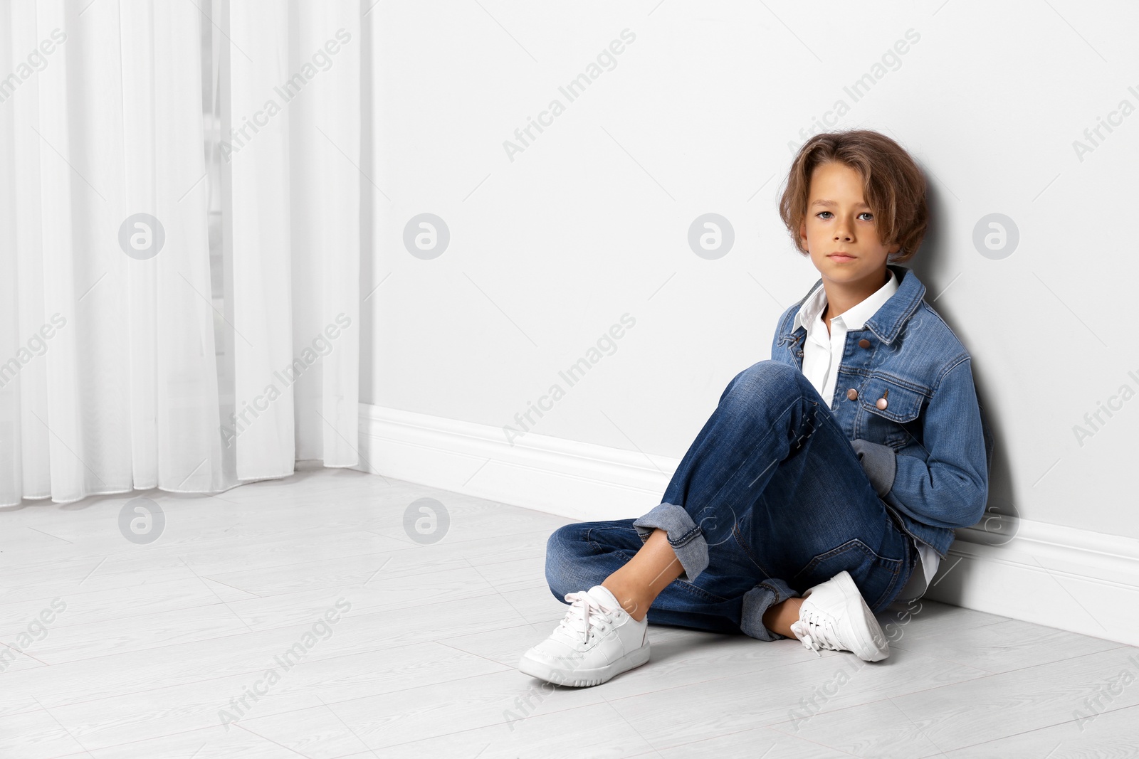 Photo of Cute little boy in casual outfit near white wall in room. Space for text