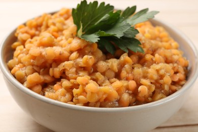 Delicious red lentils with parsley in bowl on table, closeup