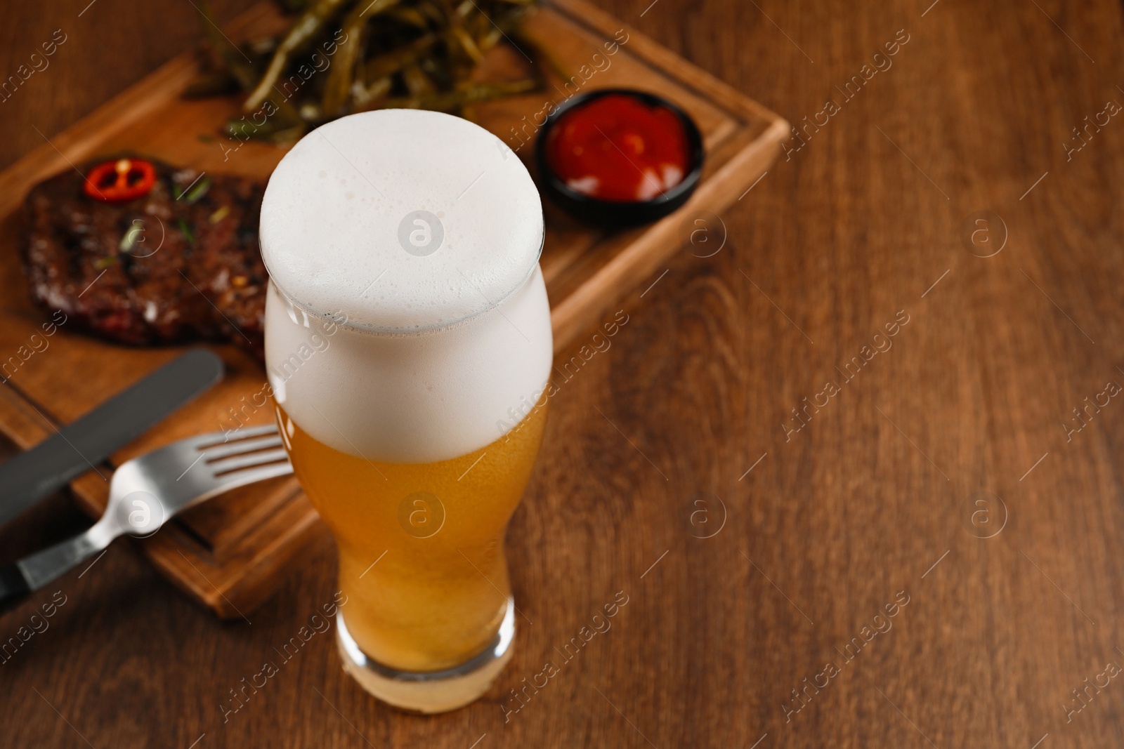 Photo of Glass of beer, delicious fried steak and sauce on wooden table. Space for text