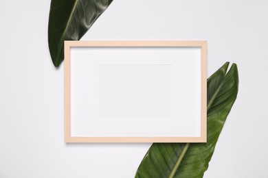 Photo of Empty photo frame and green leaves on white background, flat lay. Mockup for design