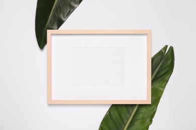 Empty photo frame and green leaves on white background, flat lay. Mockup for design