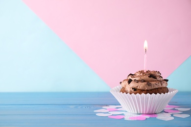 Chocolate cupcake with burning candle on blue wooden table against color background. Space for text