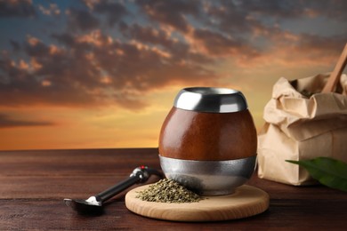 Image of Calabash with mate tea and bombilla on wooden table outdoors at sunset. Space for text