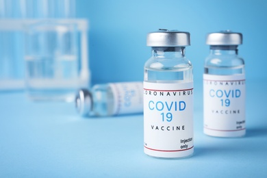 Photo of Vials with coronavirus vaccine on light blue background, space for text