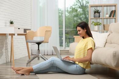 Young woman working with laptop near sofa at home, space for text